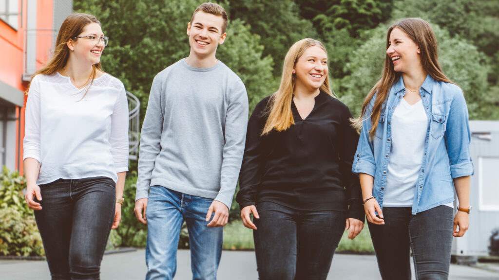 Gruppe Auszubildende von CC Pharma auf dem Innenhof und schauen sich lächelnd an.